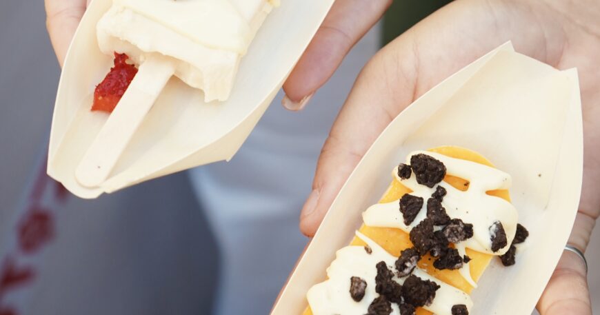 Dos paletas de helado, una con fresas y crema, y otra de mango con trozos de galleta, presentadas en bandejas de madera.