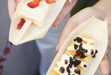 Dos paletas de helado, una con fresas y crema, y otra de mango con trozos de galleta, presentadas en bandejas de madera.